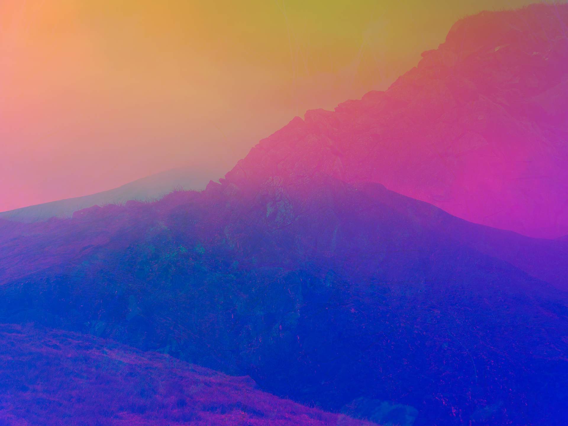 A digital collage, consisting of layers of photographic images in an array of hyper-realistic colours. Multiple photographs of mountains can be seen on top of each other. One of the mountains is slightly obscured by clouds at its peak. 