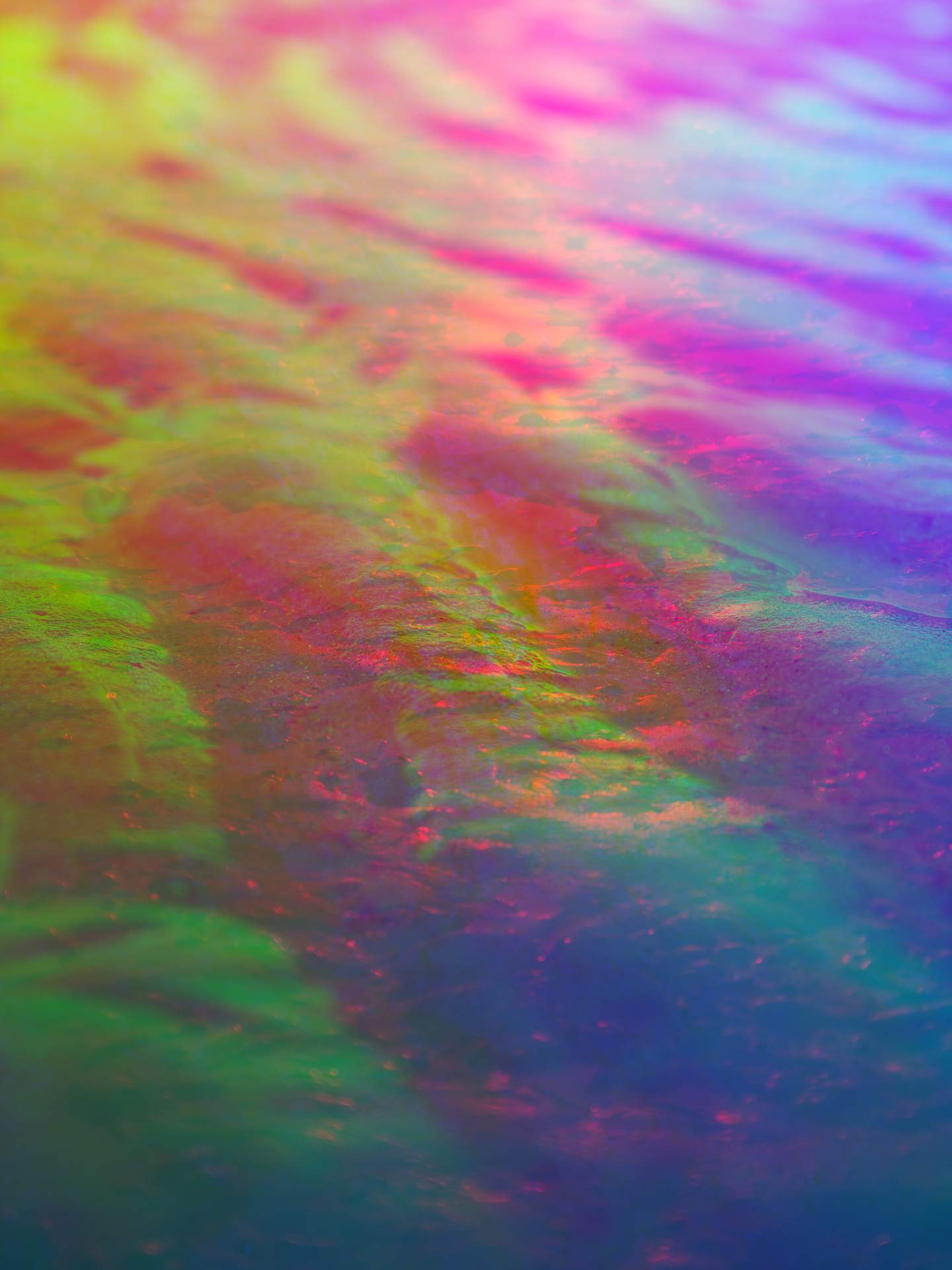 A digital collage consisting of multiple layers of photographs in an array of hyper-realistic colours. The surface of a beach can be seen, with ripples appearing in the sand from the movement of the sea.