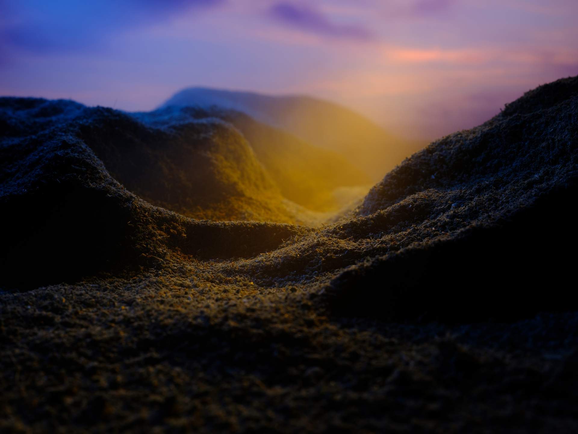An image of a valley with yellow mist appearing from behind a mountain on the right, set against an evening sky with soft clouds.
