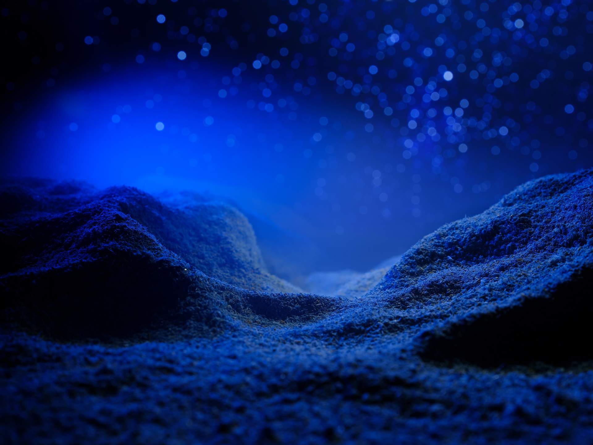An image of a hilly landscape with blue mist hovering above its surface, set against a night sky with hundreds of white stars. 
