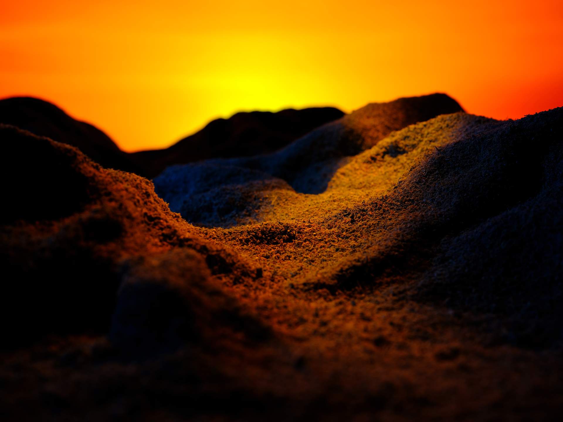 An image showing mountains in a valley, set against a rich yellow and orange sky. The centre of this landscape is highlighted in yellow light, while the rest of the landscape is shrouded in shadow.