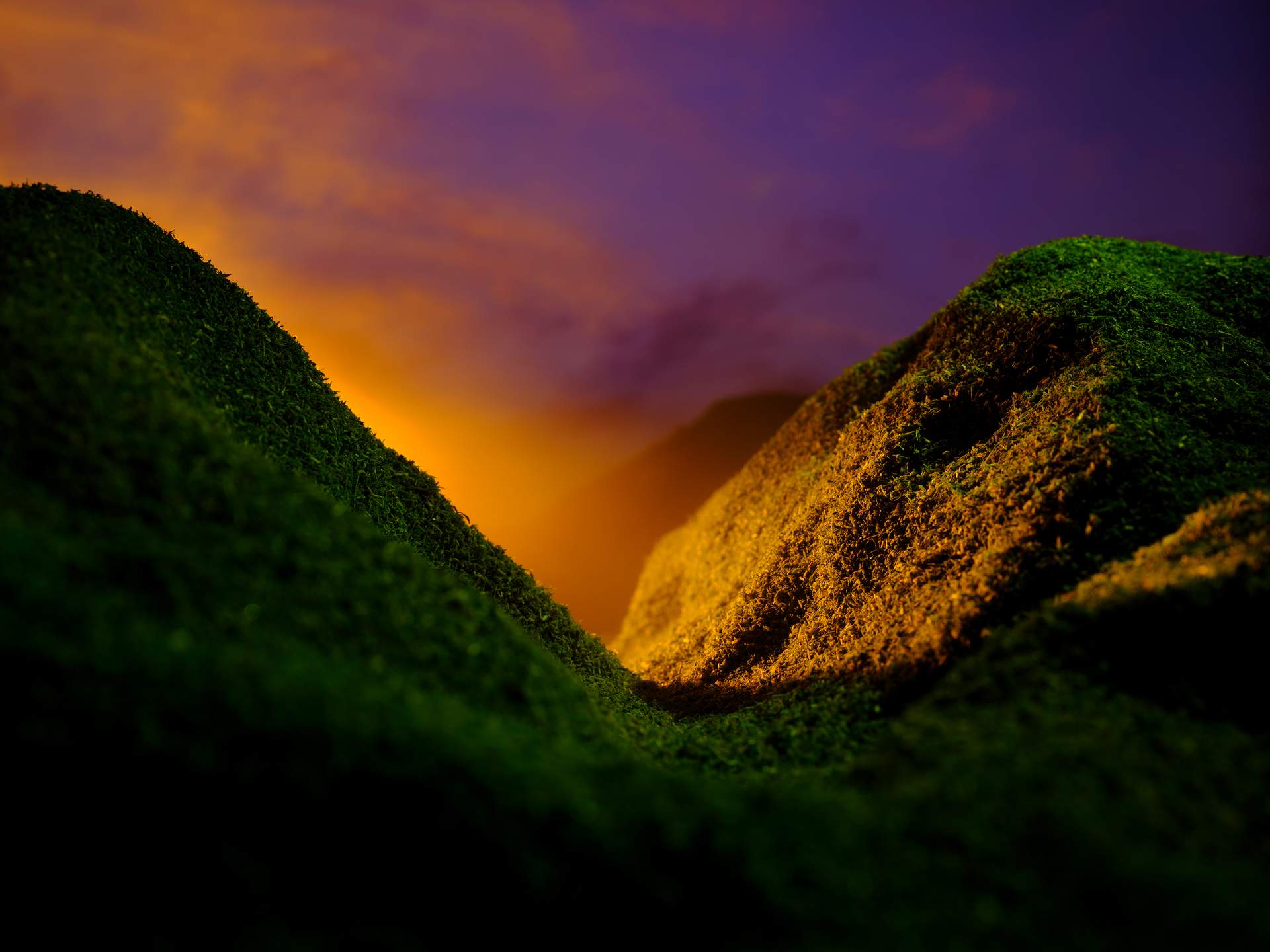 An image of a valley with yellow mist appearing from behind a mountain on the left, set against a pink and purple sunset.
