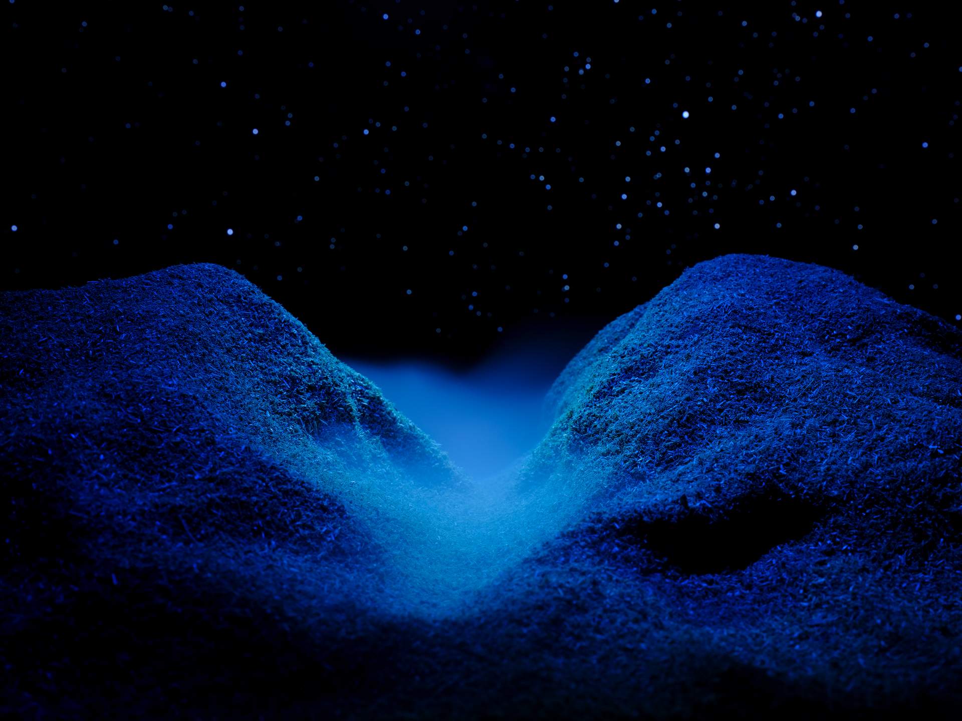 An image of a valley with blue mist at its centre, set against a night sky with hundreds of white stars. 