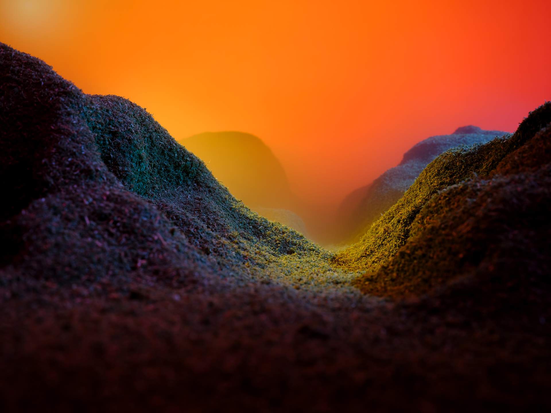 An image showing the landscape of a valley. There is a mountain in the distance shrouded in thick yellow and orange fog. The landscape in the foreground is dark blue and purple.